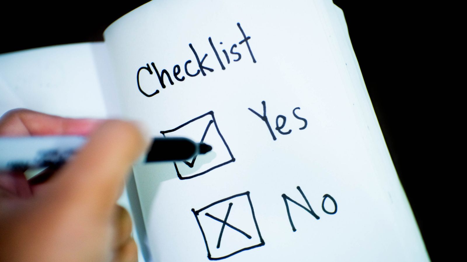 A hand marking a handwritten checklist in a notebook, ticking yes and crossing no.